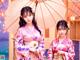 Two women in kimonos standing under an umbrella. 