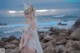 A woman in a white dress standing on a rocky beach.