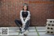 A woman sitting on the ground in front of a brick wall.