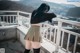 A woman standing on a balcony with her back to the camera.