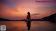 A woman sitting on the edge of a swimming pool at sunset.