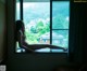 A naked woman sitting on a window sill looking out the window.