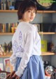 A woman in a white shirt and blue skirt standing in front of a bookshelf.