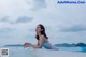 A woman in a white lingerie sitting on the edge of a swimming pool.